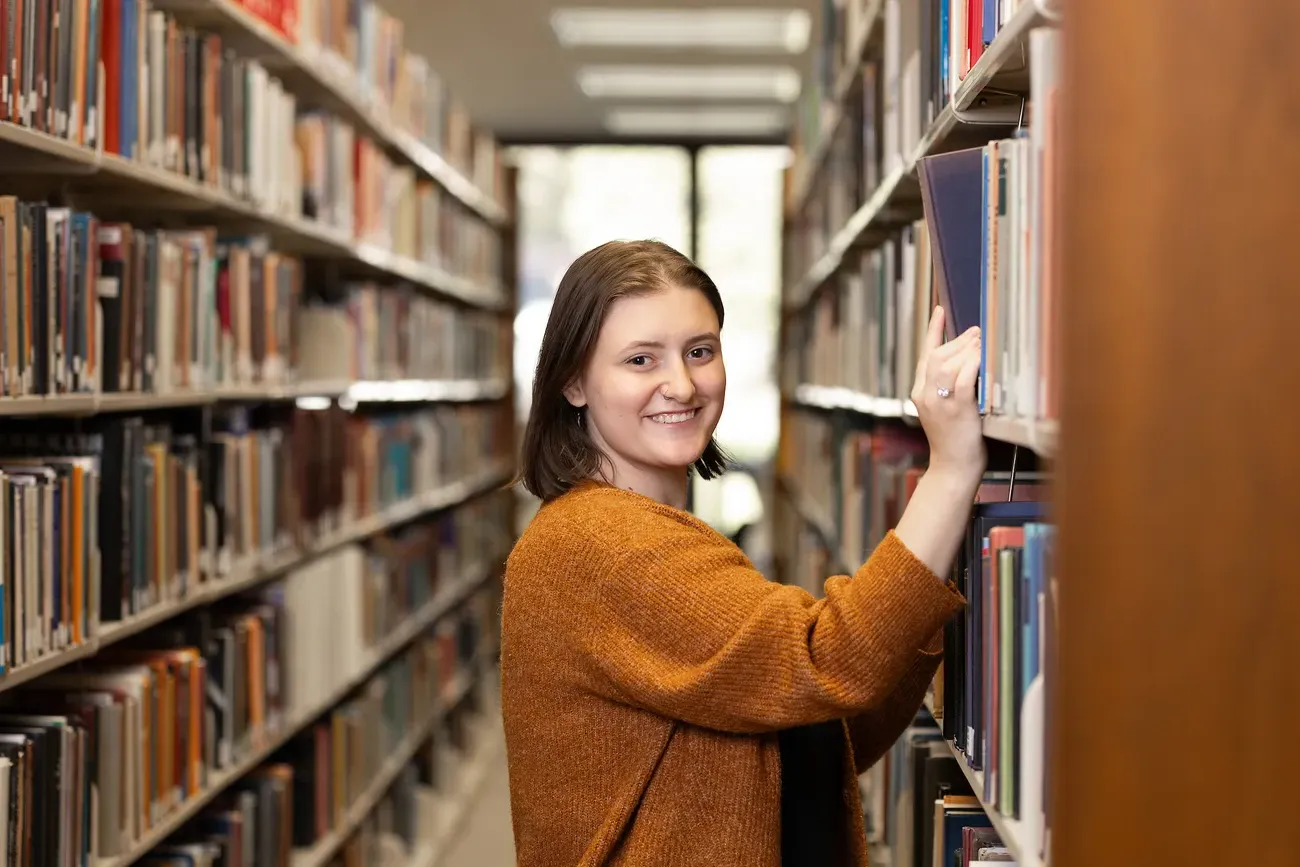 Student picks books off shelves in library.